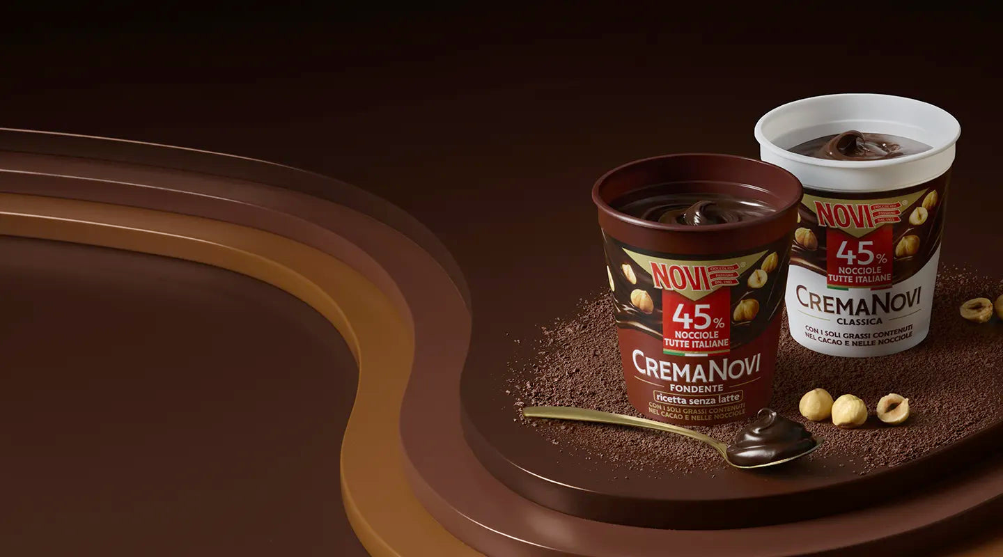 I vasetti di Crema Novi Fondente e Crema Novi Classica su un piano di cioccolato, con nocciole, cacao in polvere e un cucchiaino